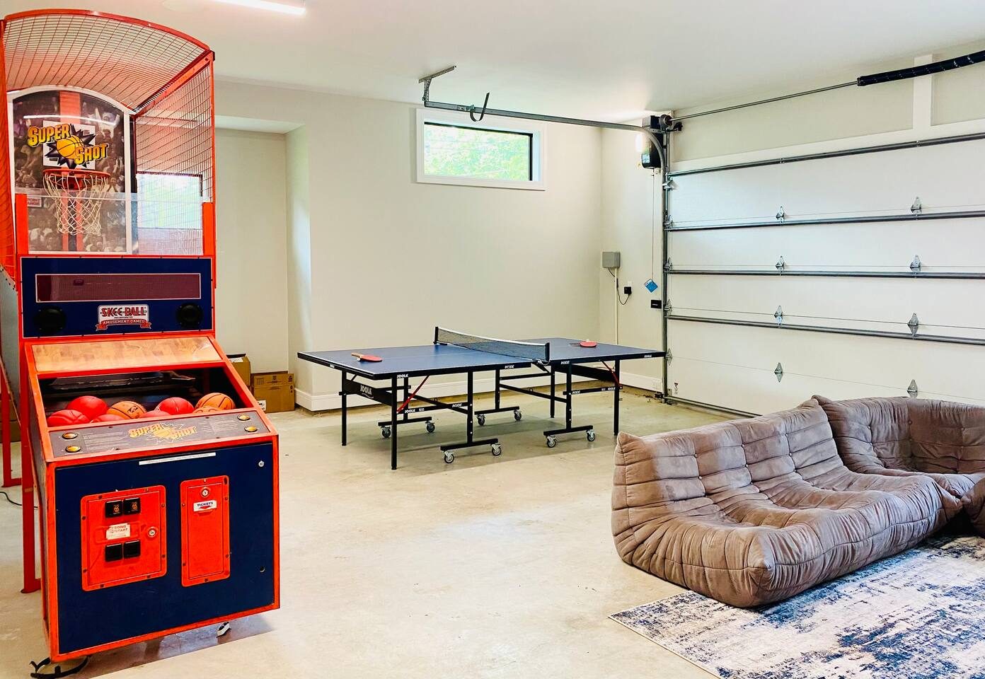 Garage game room complete with Super Shot arcade basketball game, table tennis table (equipment included), card games, kids toys, and lounger chairs.